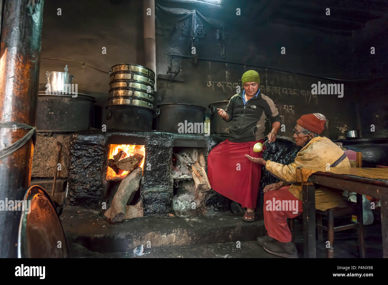 Vieux moine est assis dans la cuisine près du feu et cuire sert lui de la nourriture Banque D'Images