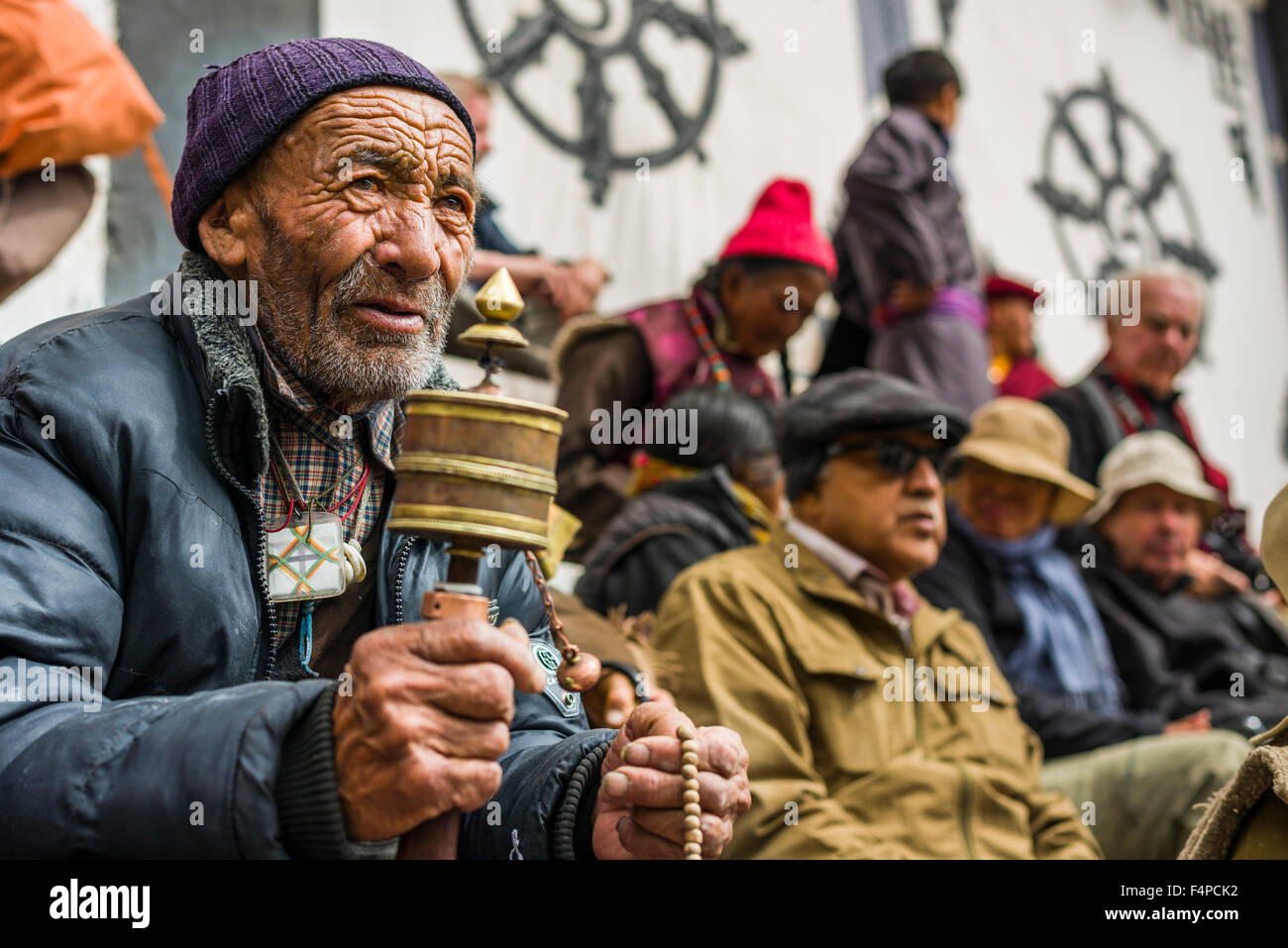 Un vieil homme ladakhis tourne un moulin à prières dans la cour d'Hemis gompa, regarder des moines avec de grands masques en bois et colorés Banque D'Images