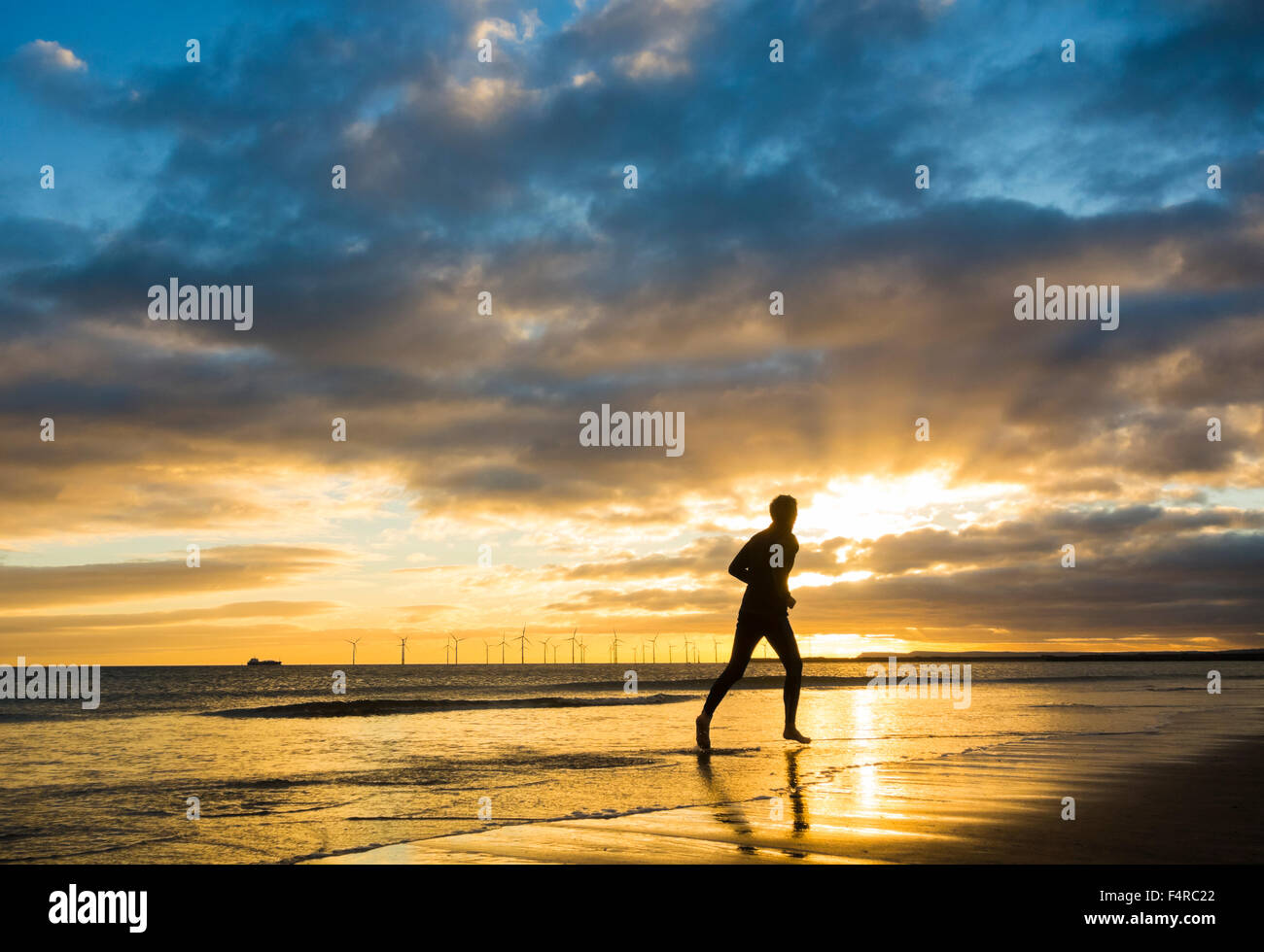 Homme mature, 50-60 ans, jogging, course sur la plage au lever du soleil. ROYAUME-UNI Banque D'Images