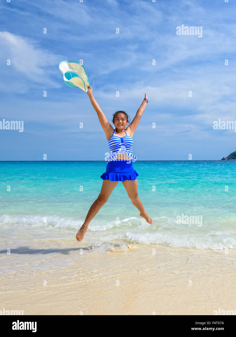 Fille de tourisme dans un maillot blanc rayé bleu en forme de saut X avec plaisir sur la belle plage et la mer en été à l'île de Koh Banque D'Images