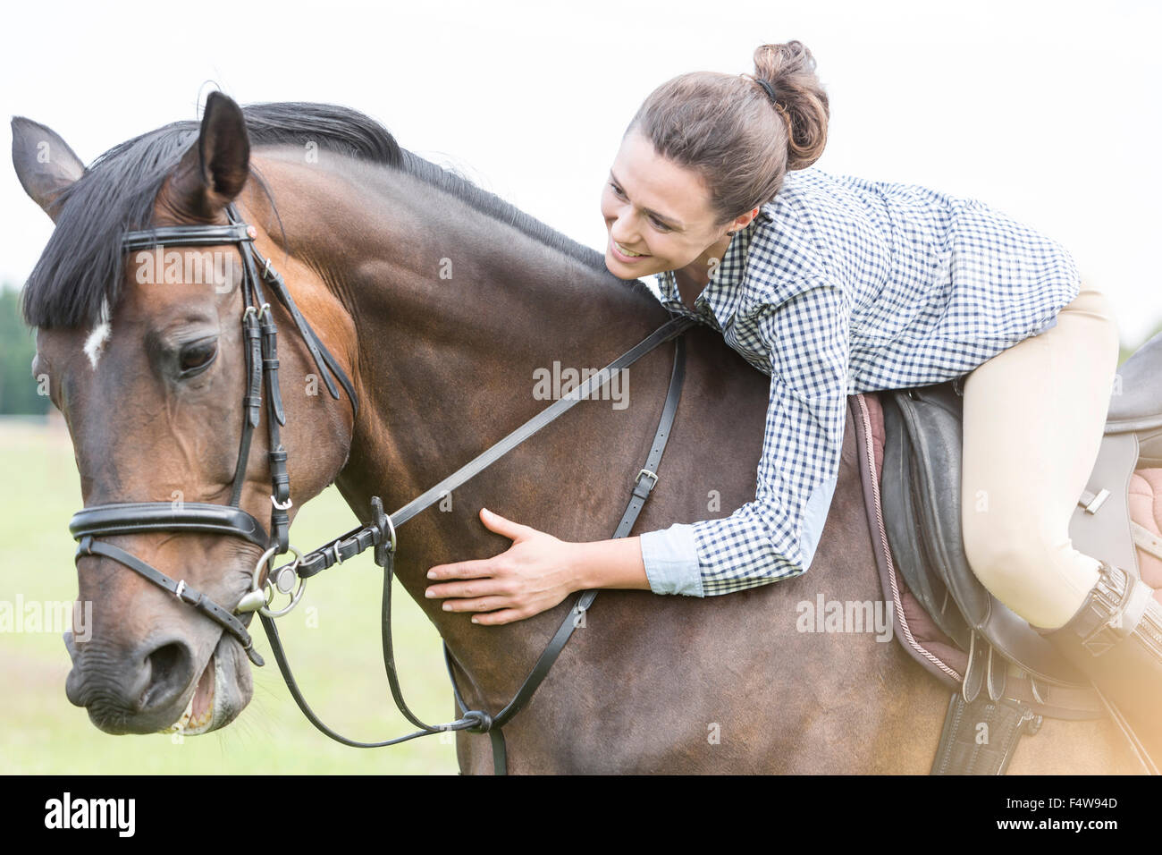 L'équitation Smiling woman leaning et petting horse Banque D'Images