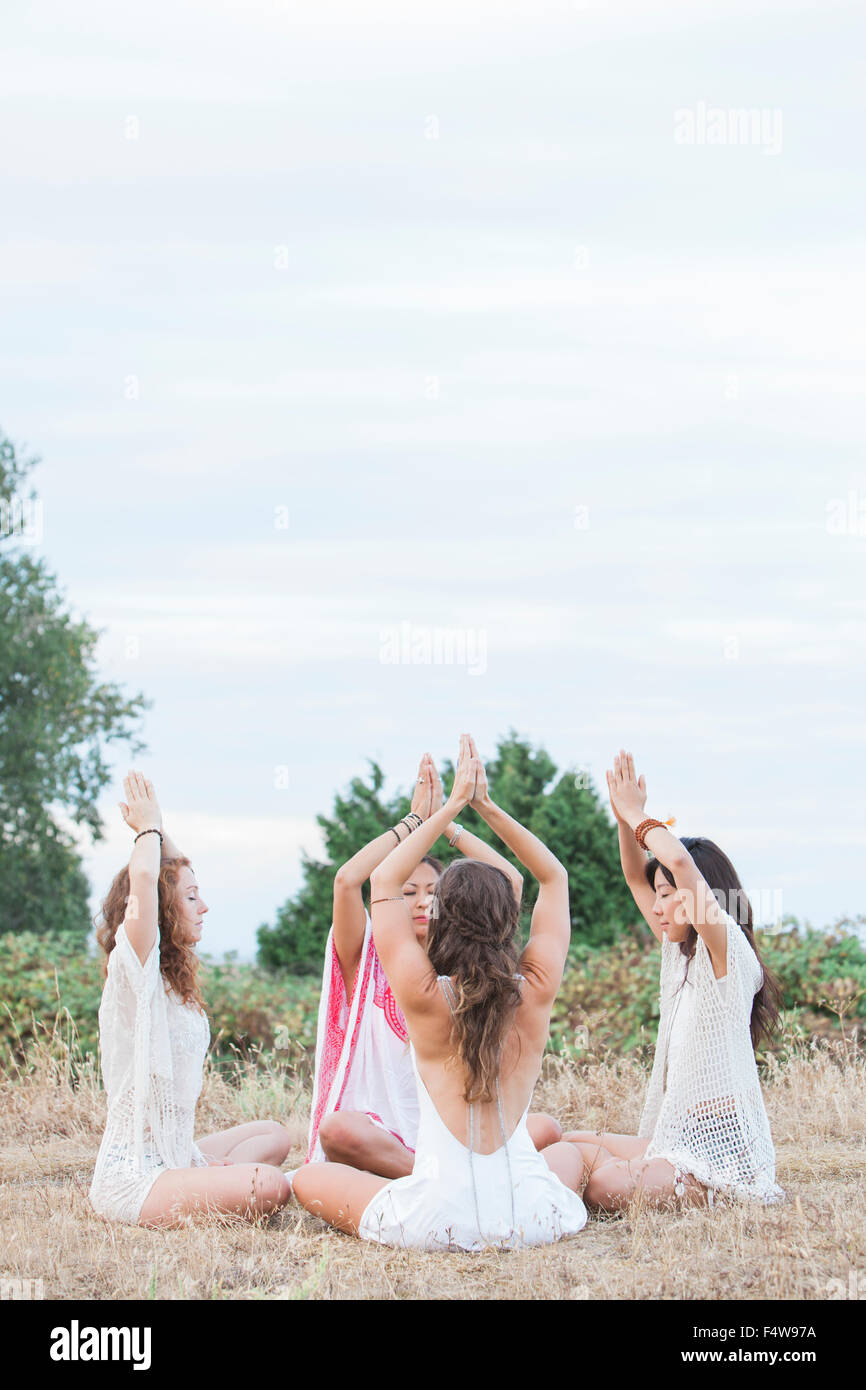 Les femmes Boho méditer avec les mains jointes en cercle au plafond in rural field Banque D'Images