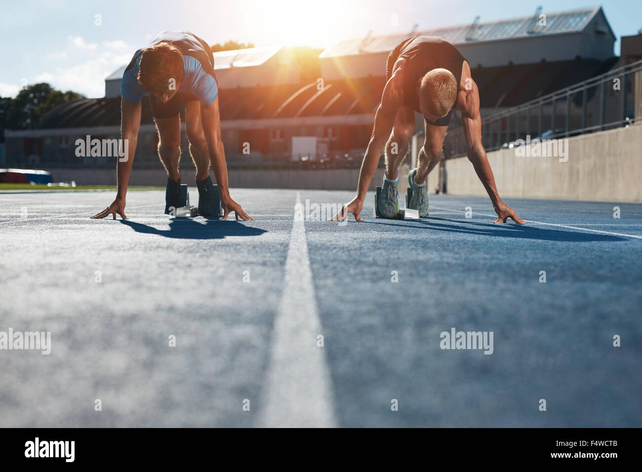 Les sprinters à blocs de départ prêt pour la race . Les athlètes à la position de départ sur le stade de l'athlétisme race track avec sun flare. Banque D'Images