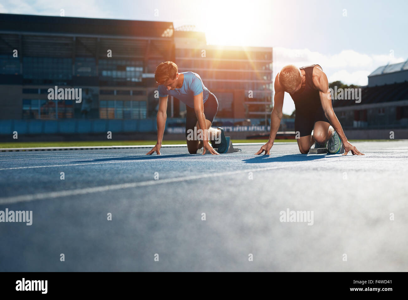 Les jeunes athlètes qui se préparent à la race dans les blocs de démarrage dans le stade. Les sprinters à blocs de départ prête pour la course avec sun flare. Banque D'Images