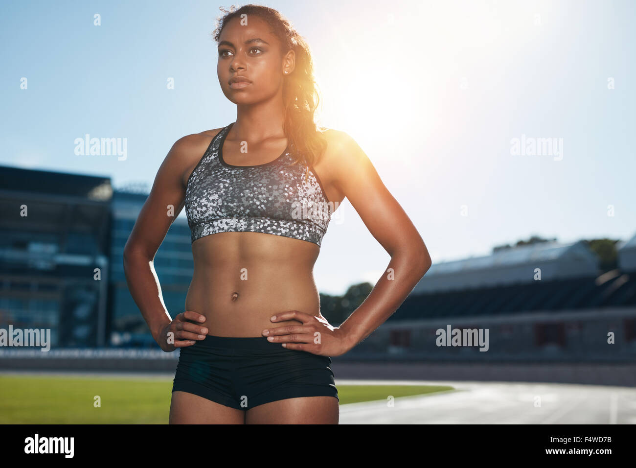 Fit young woman standing avec ses mains sur les hanches à la route. Athlète féminine de l'Afrique de se préparer à exécuter sur un stade de l'athlétisme ra Banque D'Images Fit young woman standing avec ses mains sur les hanches à la route. Athlète féminine de l'Afrique de se préparer à exécuter sur un stade de l'athlétisme ra Banque D'Images