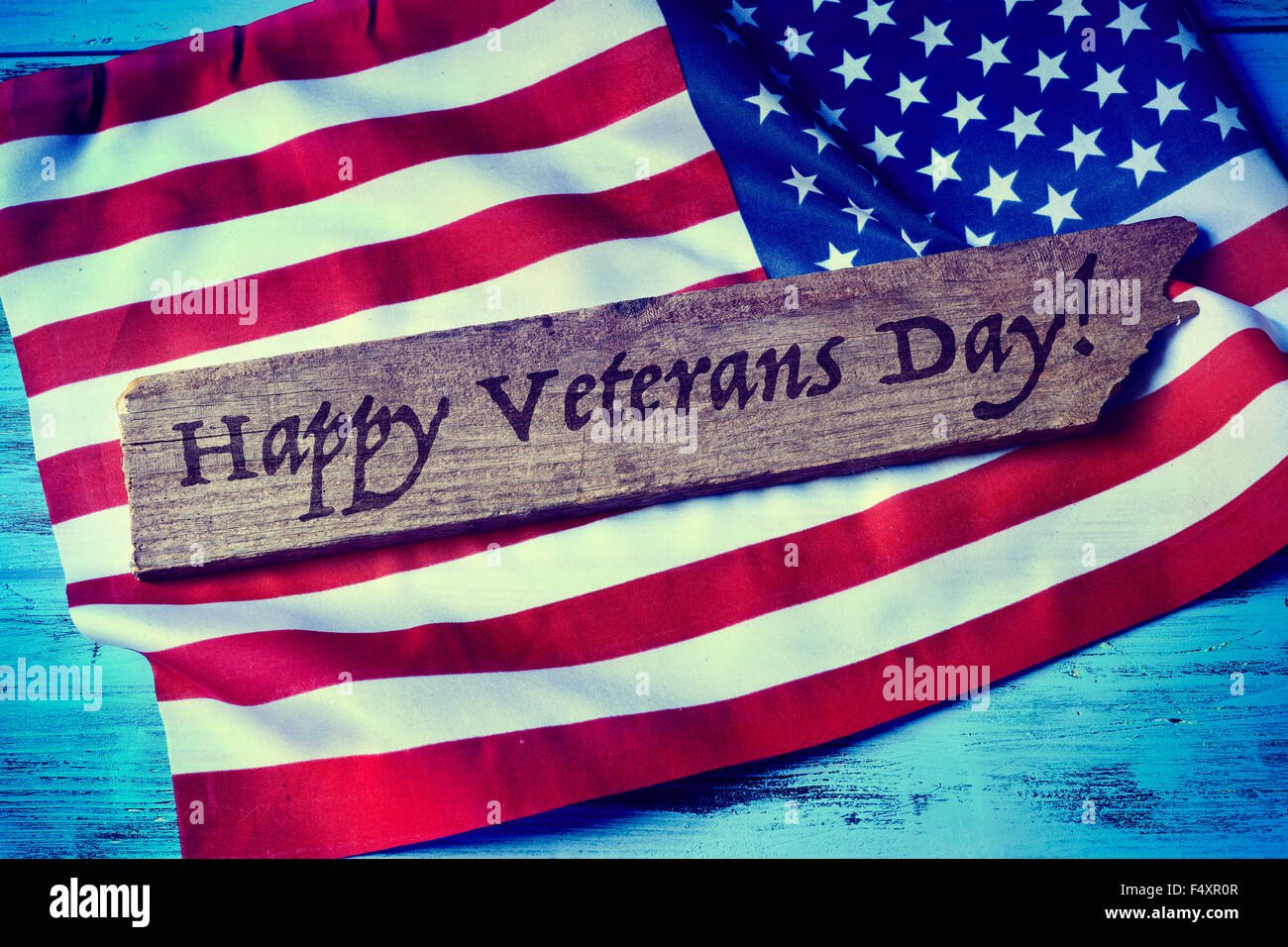 Le texte écrit de jour de vétérans heureux dans un morceau de bois et un drapeau des États-Unis, sur un fond bleu en bois rustique Banque D'Images