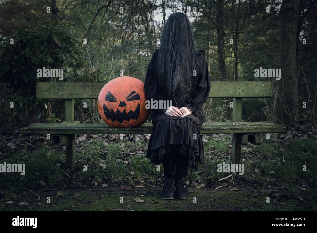 Femme en noir, le visage recouvert de longs cheveux noirs, assis à côté d'une citrouille, fantôme femme avec tête de citrouille, Halloween Banque D'Images