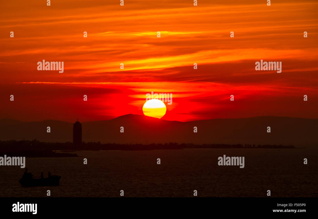 Soleil brûlant descend derrière les collines au loin comme un bateau navigue dans la photo Banque D'Images