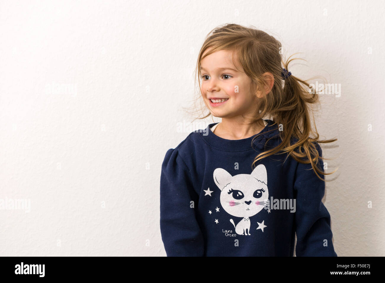 Un Portrait of a smiling fillette de trois ans avec les cheveux blonds, vêtu d'un pull bleu avec la photo d'un chat blanc Banque D'Images