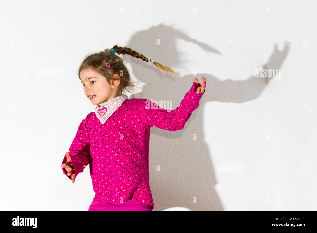 Une blonde fillette de trois ans, porter un chandail rose, c'est danser devant un mur blanc, laissant son ombre derrière elle Banque D'Images