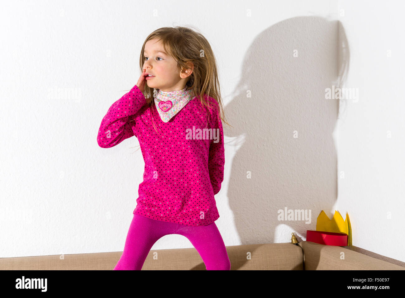 Une blonde fillette de trois ans, porter un chandail rose, danse avec cheveux ouvert devant un mur blanc, laissant son ombre derrière Banque D'Images