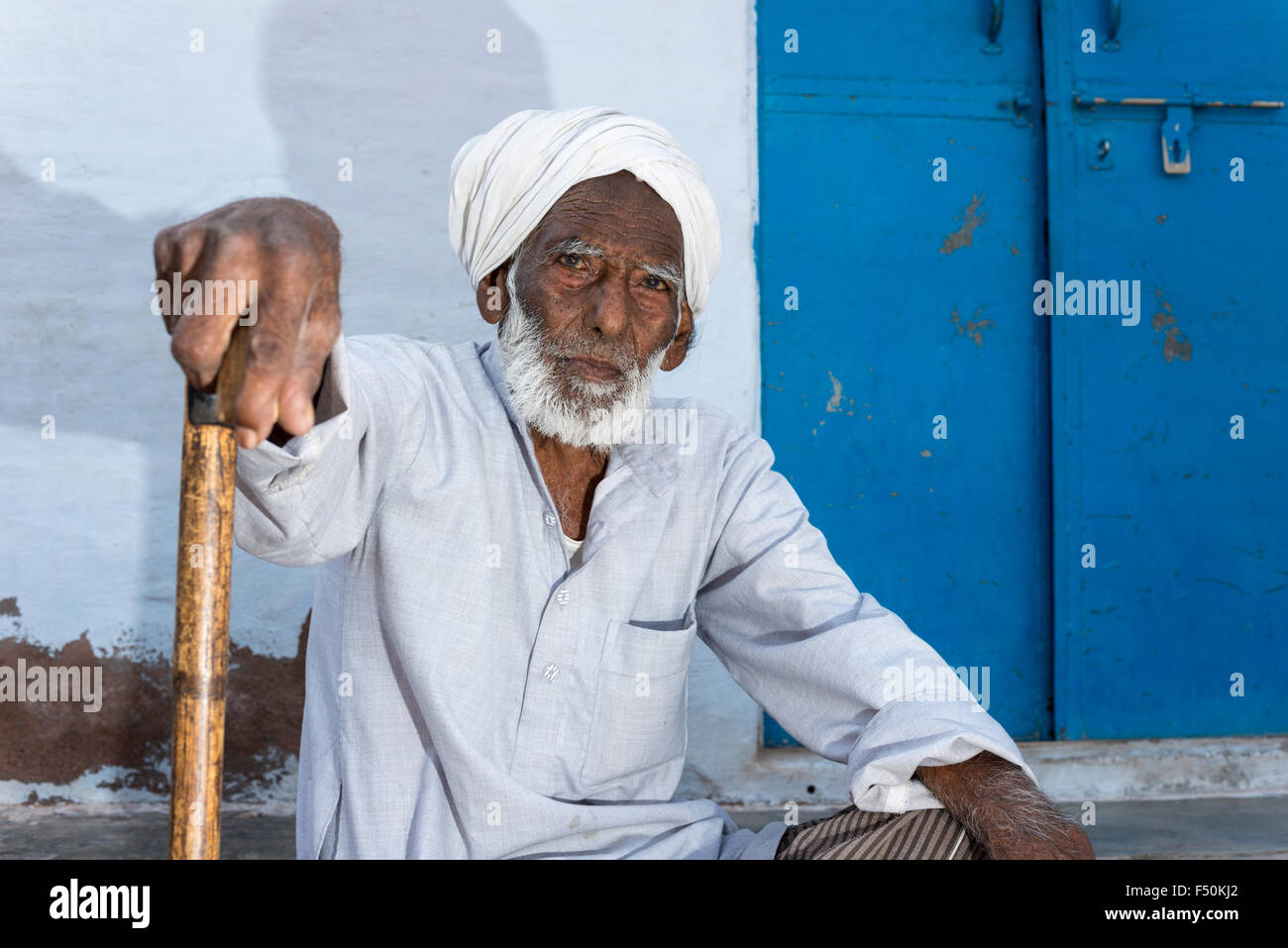 Un vieil homme avec une barbe grise tourban blanc est assis en face de sa maison Banque D'Images