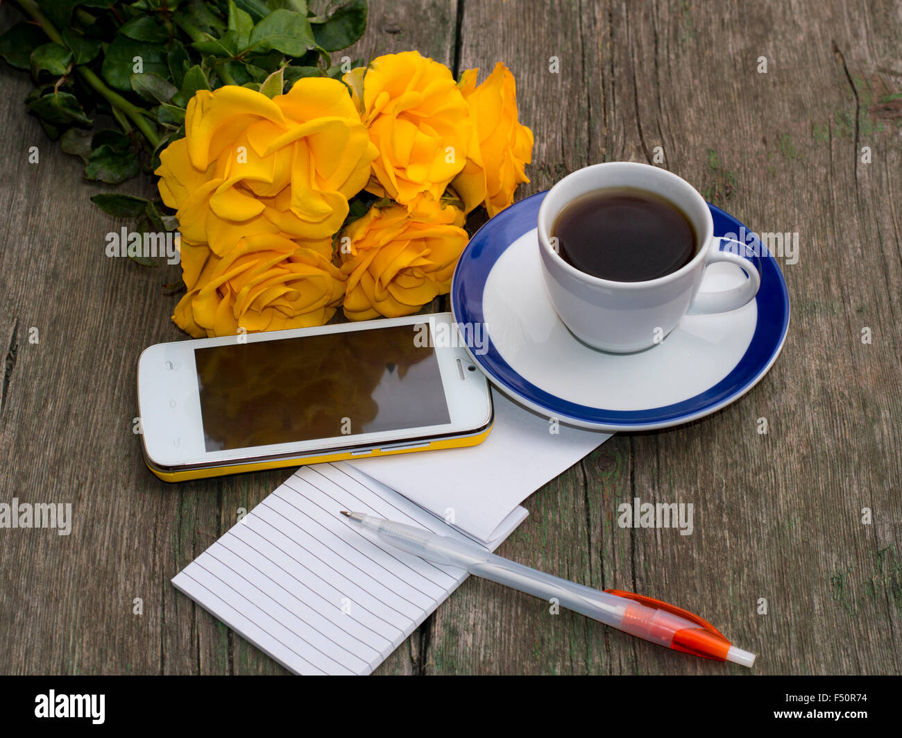 Tasse de café, le bouquet de roses jaunes, d'un téléphone, de la poignée, la vue de dessus, sur une table en bois, une nature morte, un objet beau fl Banque D'Images