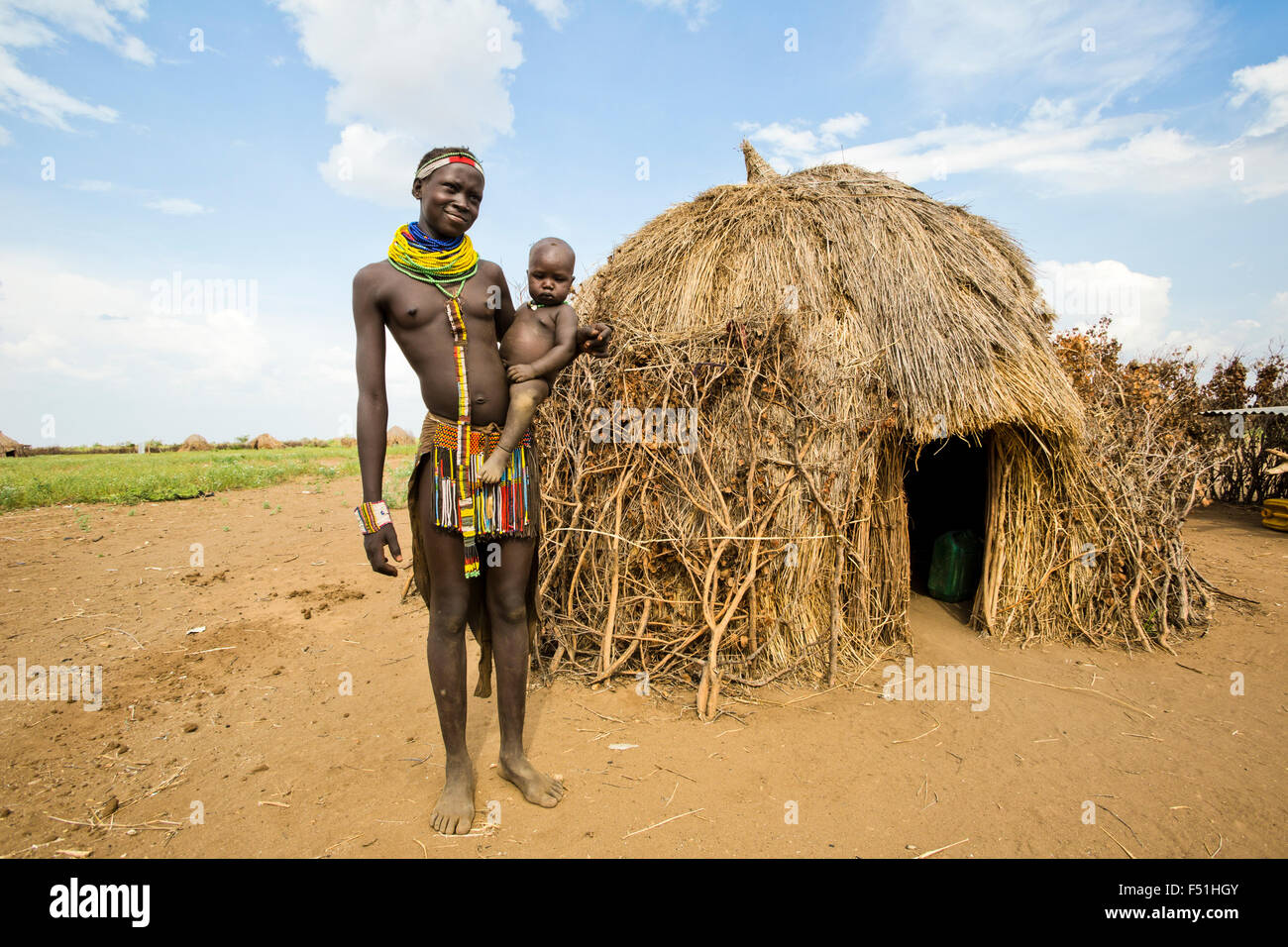 Jeune femme Nyangatom avec bébé dans les bras, se tient à côté de sa cabane de chaume. Vallée de l'Omo, Ethiopie Banque D'Images
