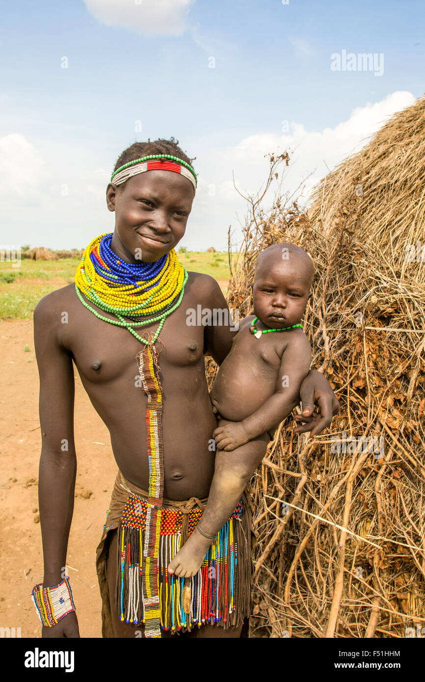 Jeune femme Nyangatom avec bébé dans les bras, se tient à côté de sa cabane de chaume. Vallée de l'Omo, Ethiopie Banque D'Images