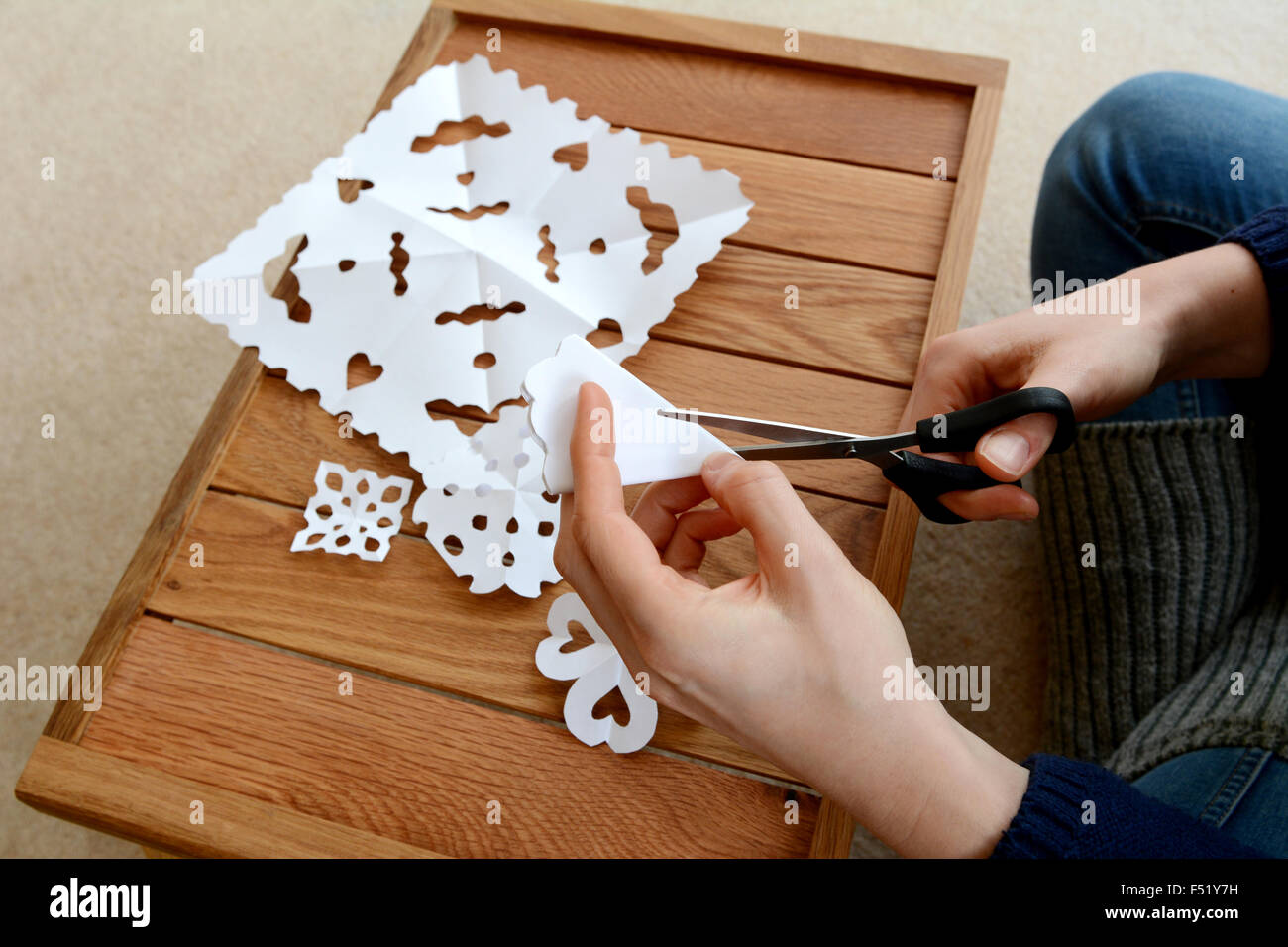 Femme à l'aide de ciseaux pour couper le papier blanc plié en dessins flocon Banque D'Images