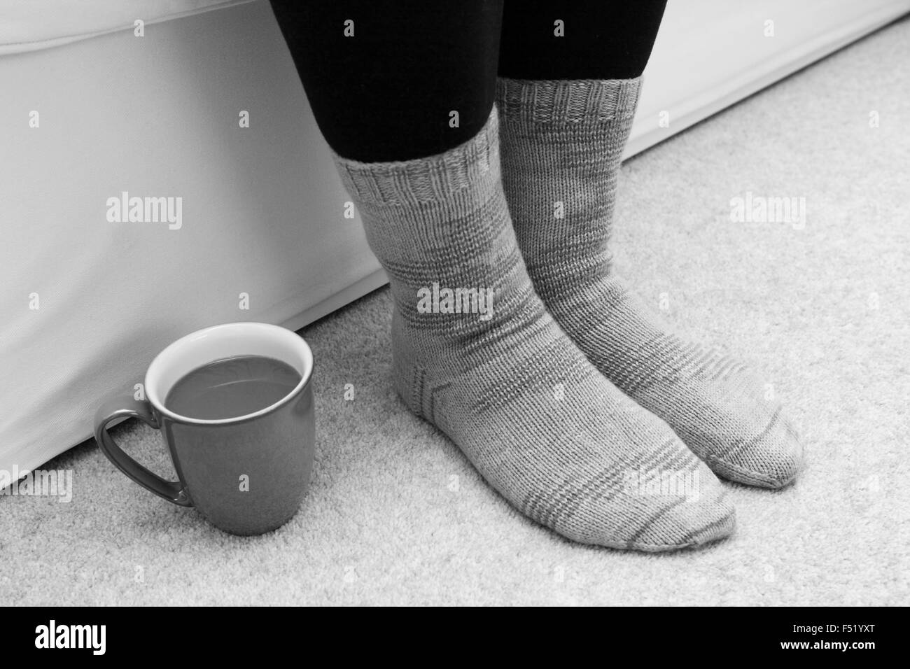 Tasse de thé ou de café sur le sol par une femme dans les pieds - chaussettes tricotées traitement monochrome Banque D'Images
