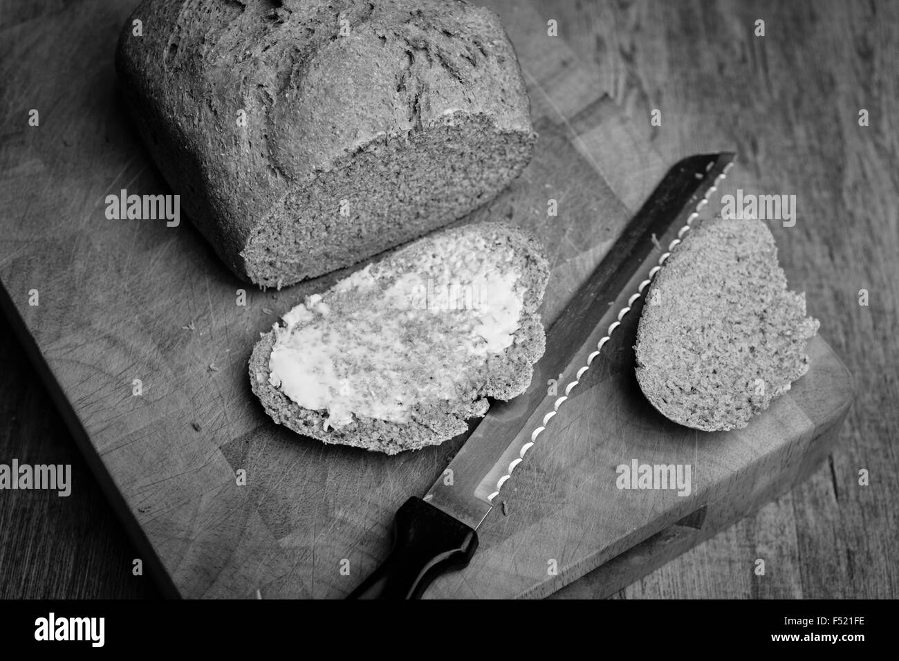 Miche de pain fraîchement cuit au four avec une tranche beurrée en noir et blanc Banque D'Images