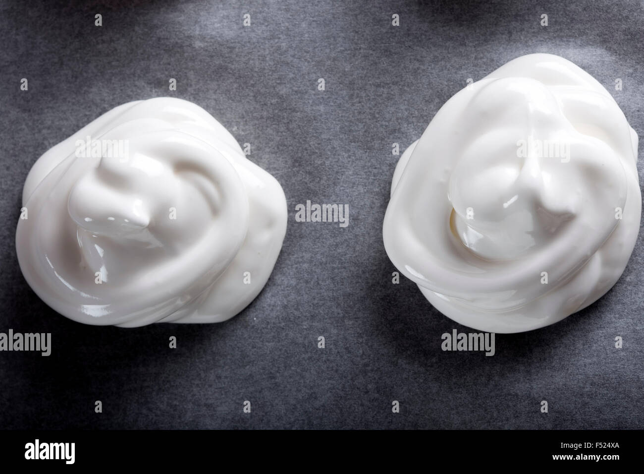 Meringues blanc sur du papier sulfurisé sur une plaque à pâtisserie Banque D'Images