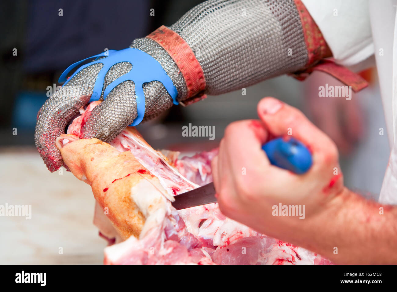 Butcher que couper la viande de porc fraîche en portant des gants protecteurs Banque D'Images