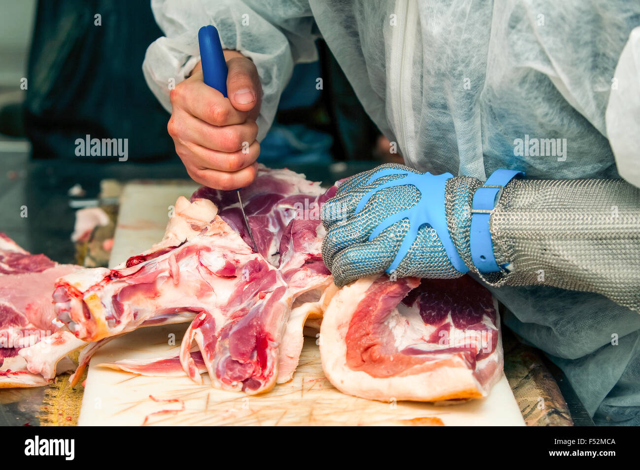 Butcher que couper la viande de porc fraîche en portant des gants protecteurs Banque D'Images