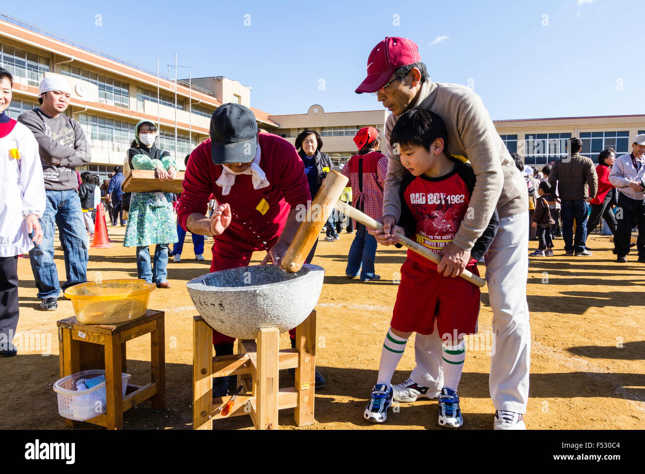 Le Japon. Omochi, riz bashing festival. Les cadres supérieurs de l'ordre de  l'homme enfant, garçon, 5-6 ans, pour aider à tenir un Kine, mallet pour  battre le riz dans un pilon. Piscine