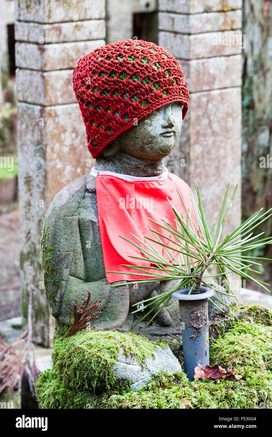 Le Japon, Koyasan, Okunoin cemetery. Petit coin de pierre-Jizo bosatsu statue bouddhiste avec soumission rouge et red hat tricoté en face de moss couverts memorial. Banque D'Images