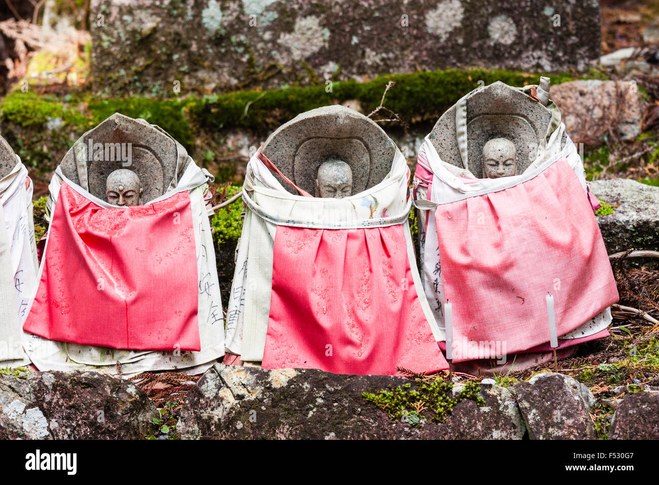 Le Japon, Koyasan, Okunoin cemetery. Trois Jizo bosatsu pierre-statue avec bavettes sur rouge, disposées en ligne sur pierre avec un peu plus de mousse derrière. Banque D'Images
