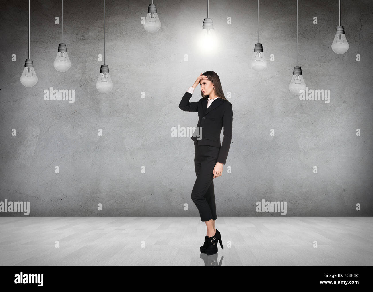 Femme stnads d'affaires dans une salle grise avec ampoules suspendues Banque D'Images