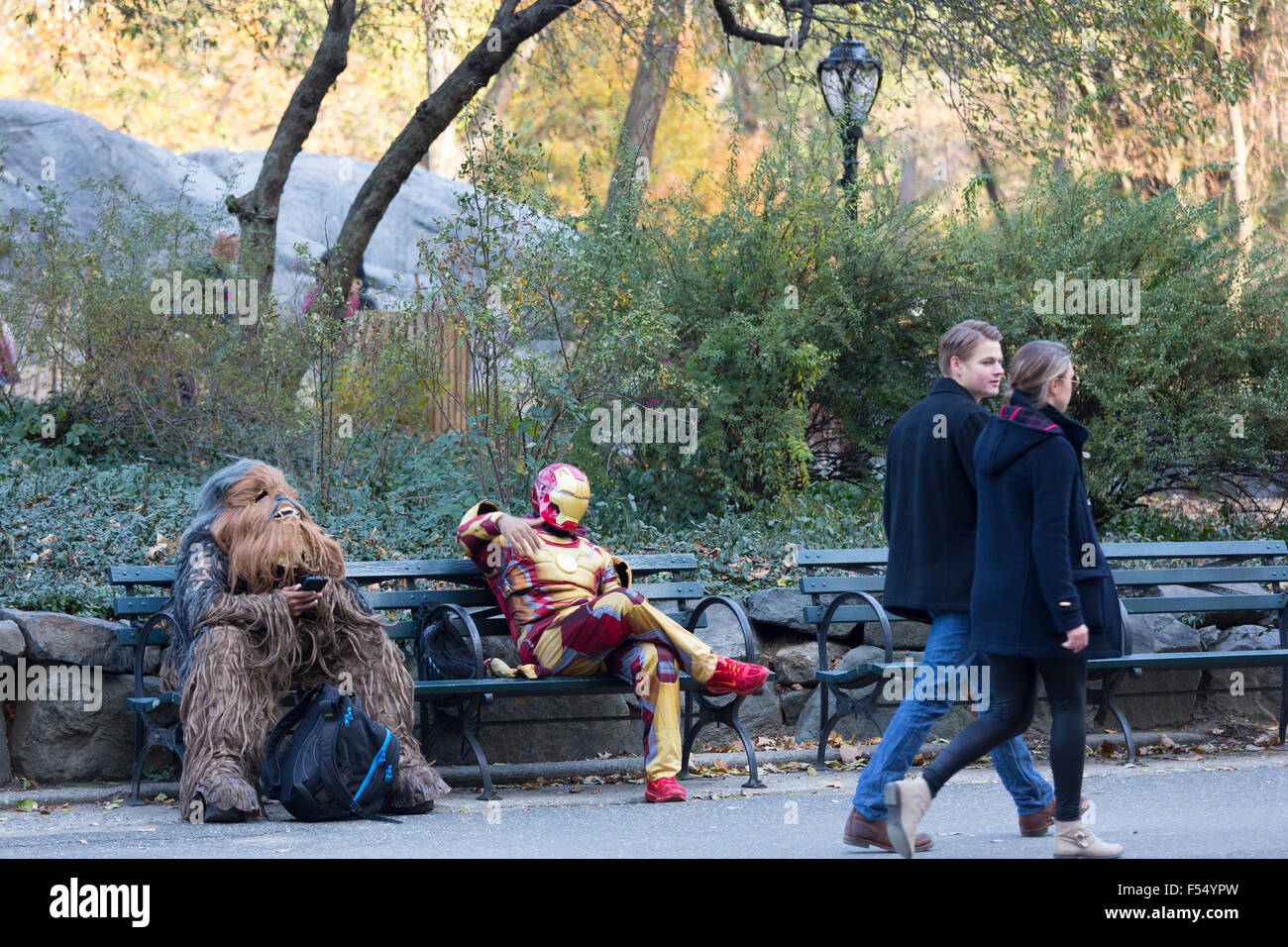 Film personnages en costume se détendre sur banc de parc comme couple marche passé en hiver dans Central Park, New York, USA Banque D'Images
