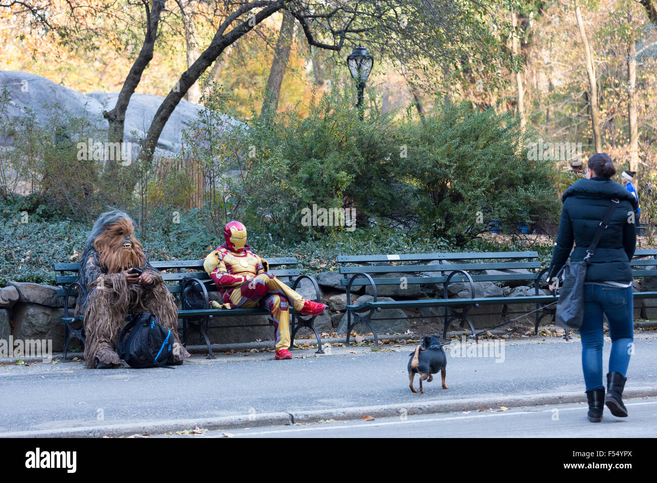 Film personnages en costume se détendre sur banc de parc comme femme passe un chien marche dans Central Park, New York, USA Banque D'Images