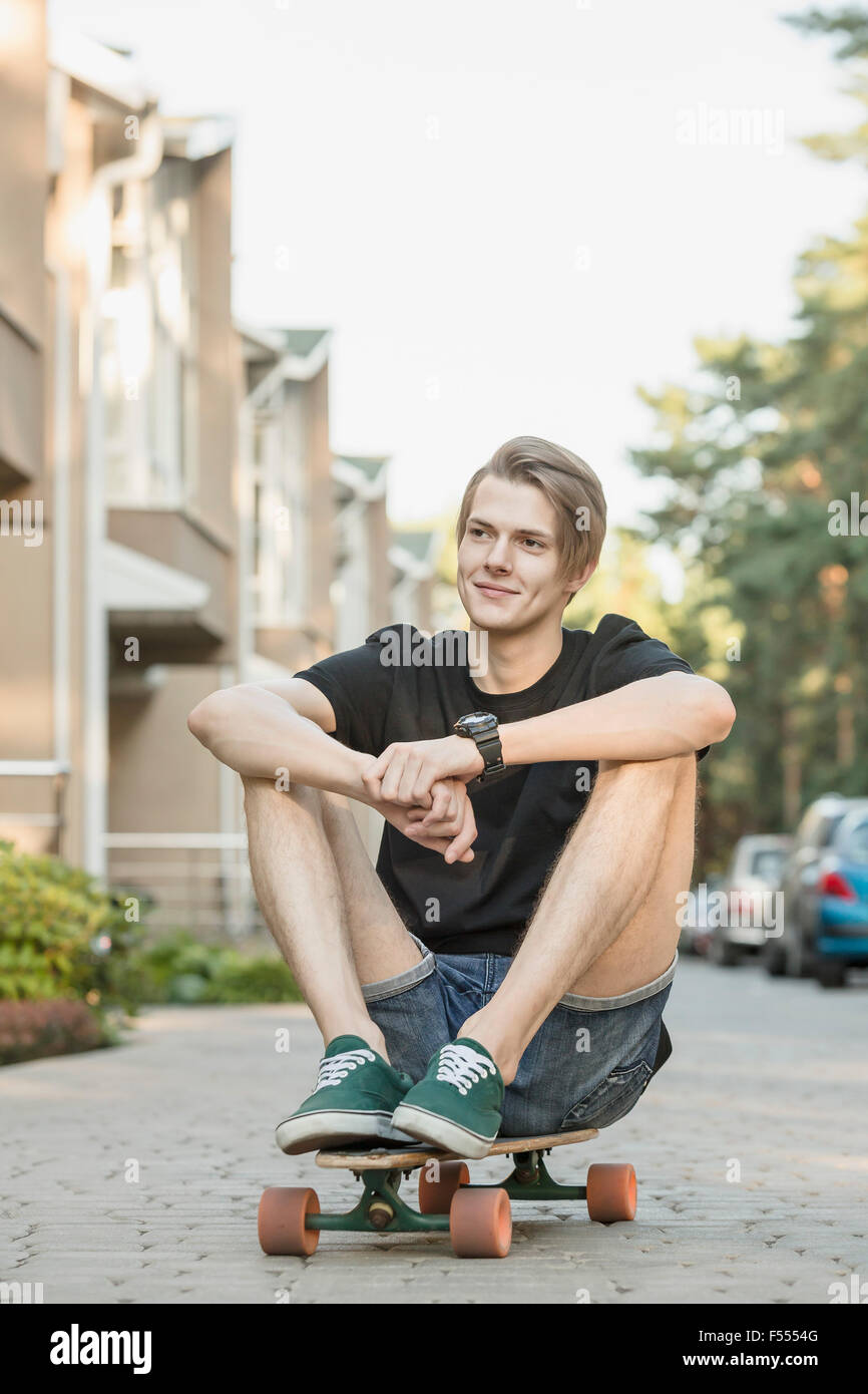 Young man sitting on skateboard en plein air Banque D'Images