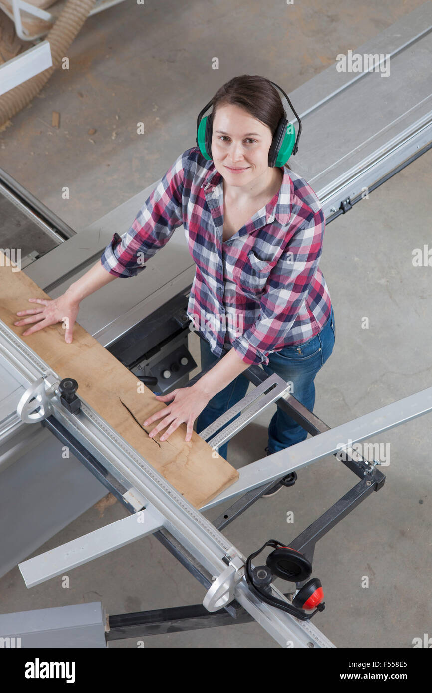 High angle portrait of happy female Carpenter à l'aide d'une scie sur table coulissante en atelier Banque D'Images
