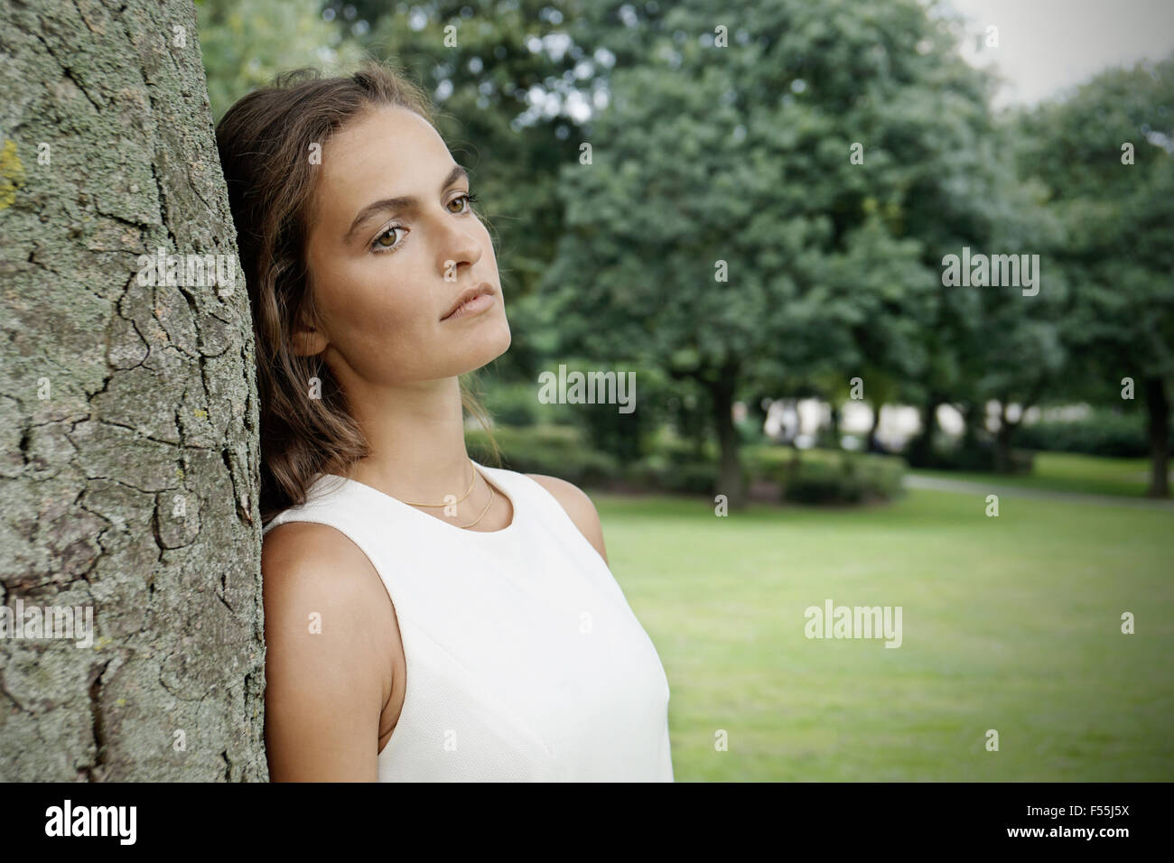 Sad young woman leaning against tree Banque D'Images