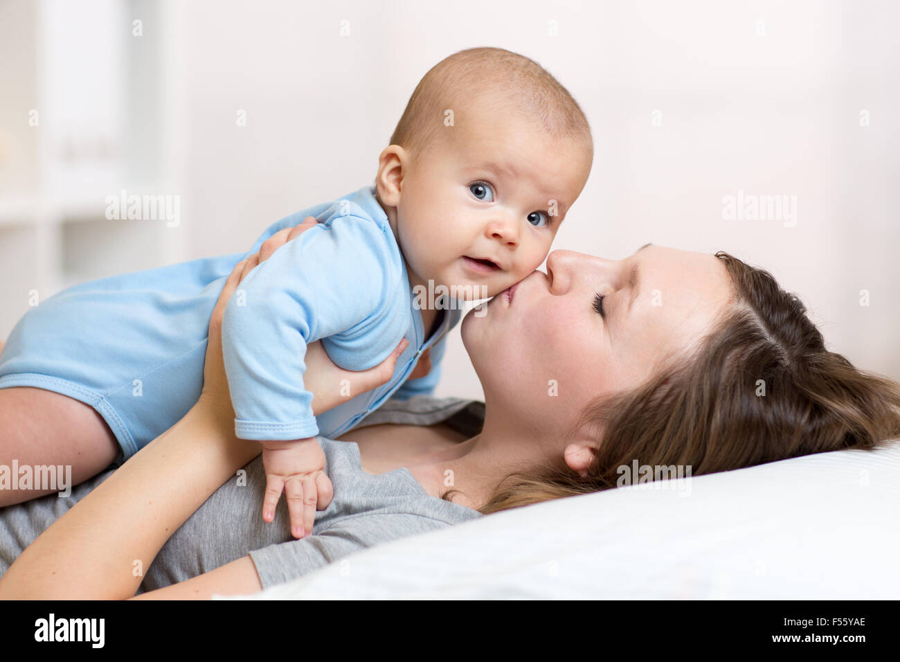 Mother kissing baby lying on bed in nursery Banque D'Images
