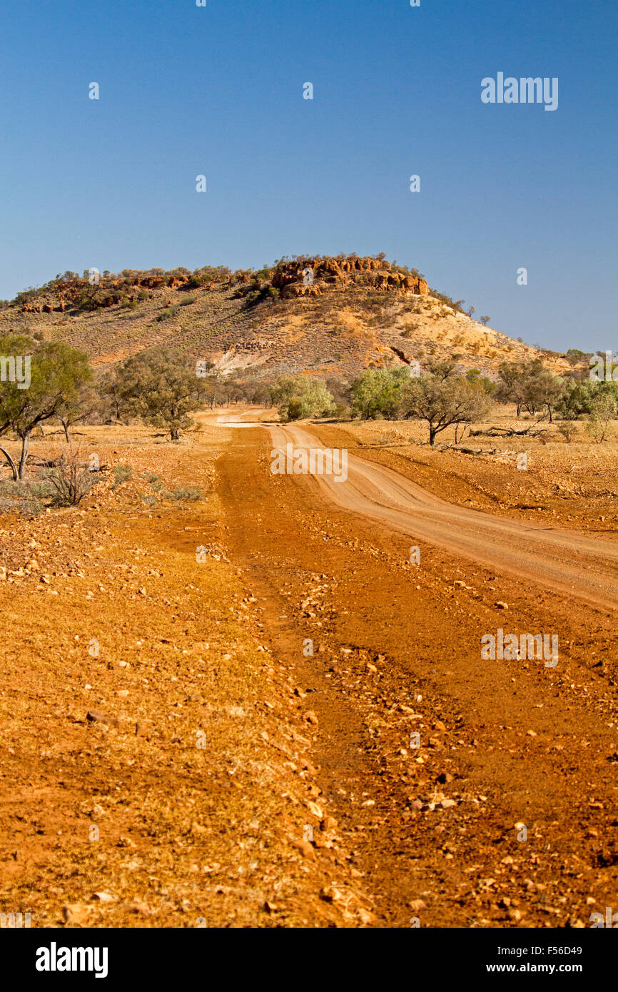 Route à travers l'Outback aride paysage caillouteux rouge avec arbres & télévision surmonté hill / mesa sur horizon lointain sous ciel bleu en Australie Banque D'Images