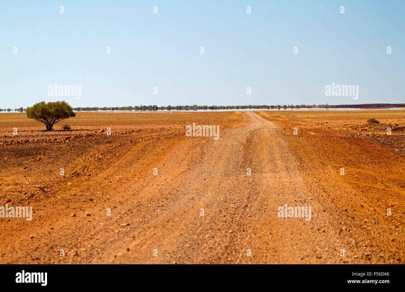 Outback long chemin de terre à travers des plaines sans arbres avec mirage rouge sur l'horizon lointain sous ciel bleu dans l'ouest du Queensland en Australie Banque D'Images