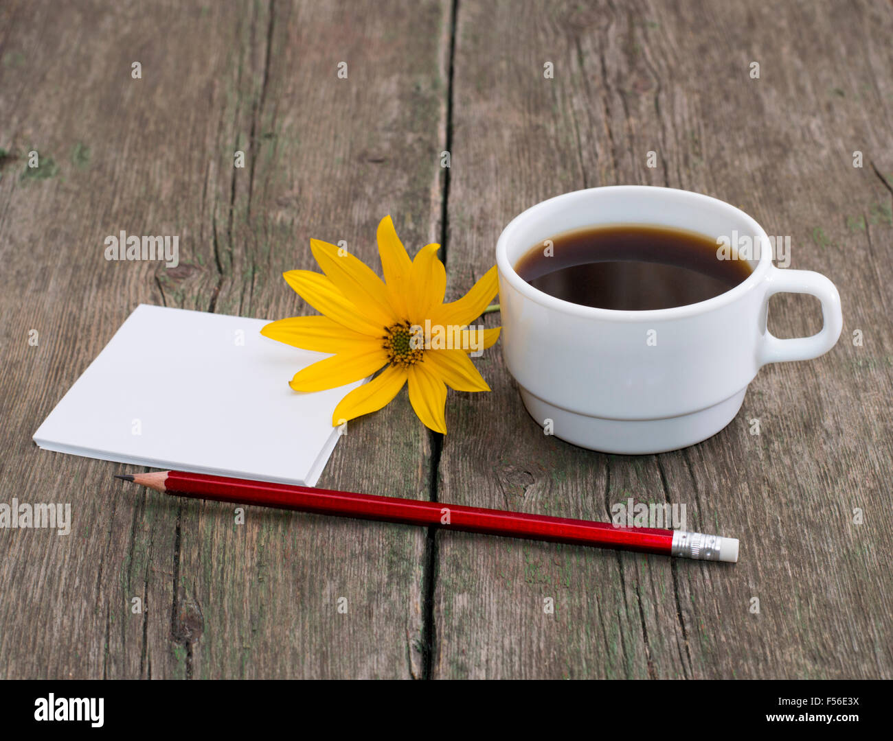 Tasse de café, un crayon à papier et une fleur jaune, une nature morte, sur une table en bois Banque D'Images