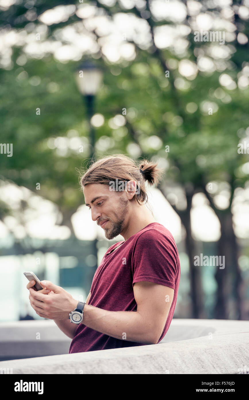 Un jeune homme dans un parc contrôler son téléphone cellulaire Banque D'Images