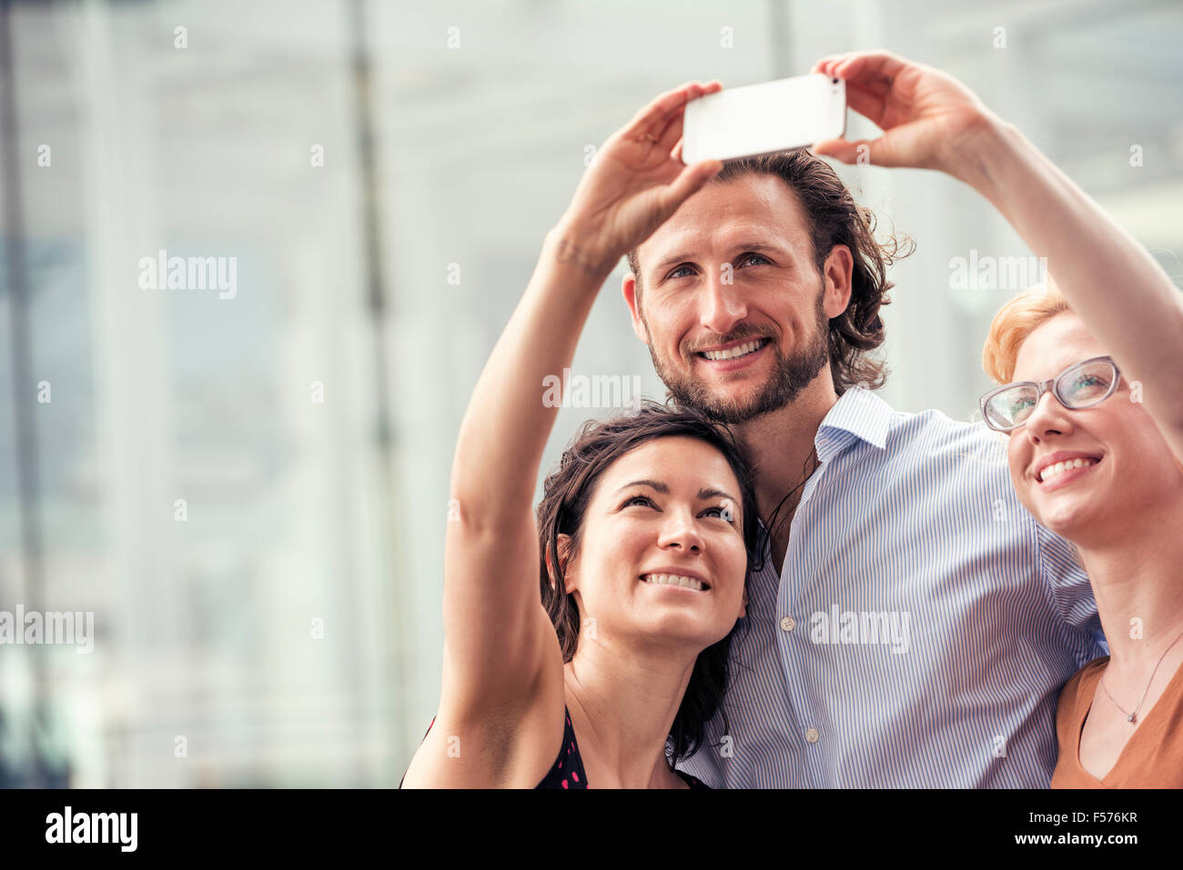 Un homme et deux femmes sur une rue de la ville, en tenant un téléphone intelligent avec un selfies. Banque D'Images