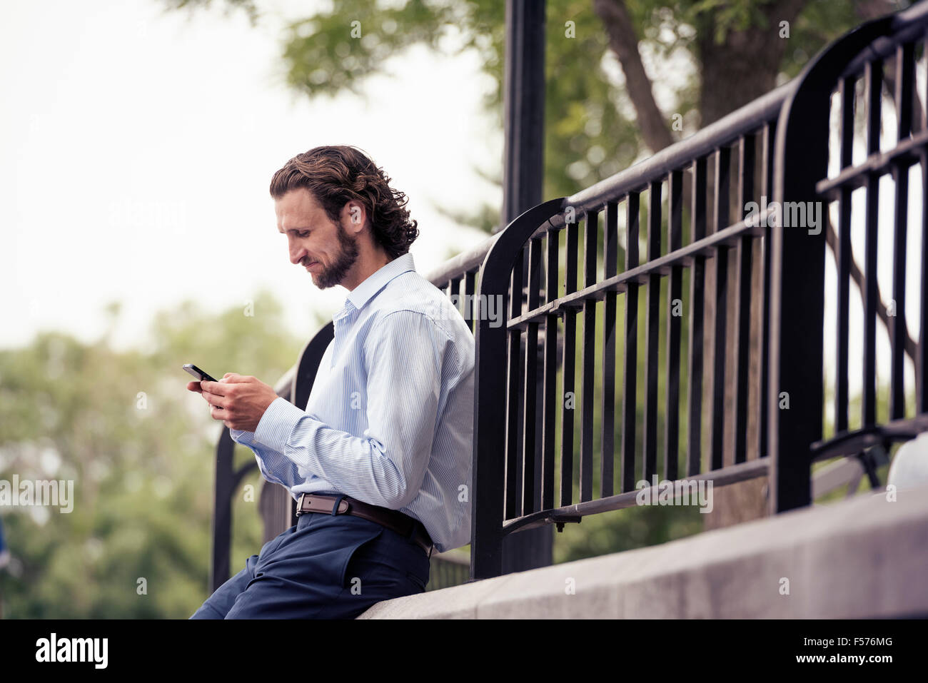 Un homme s'arrêtant dans la rue, assis sur un pas contrôler son téléphone cellulaire. Banque D'Images