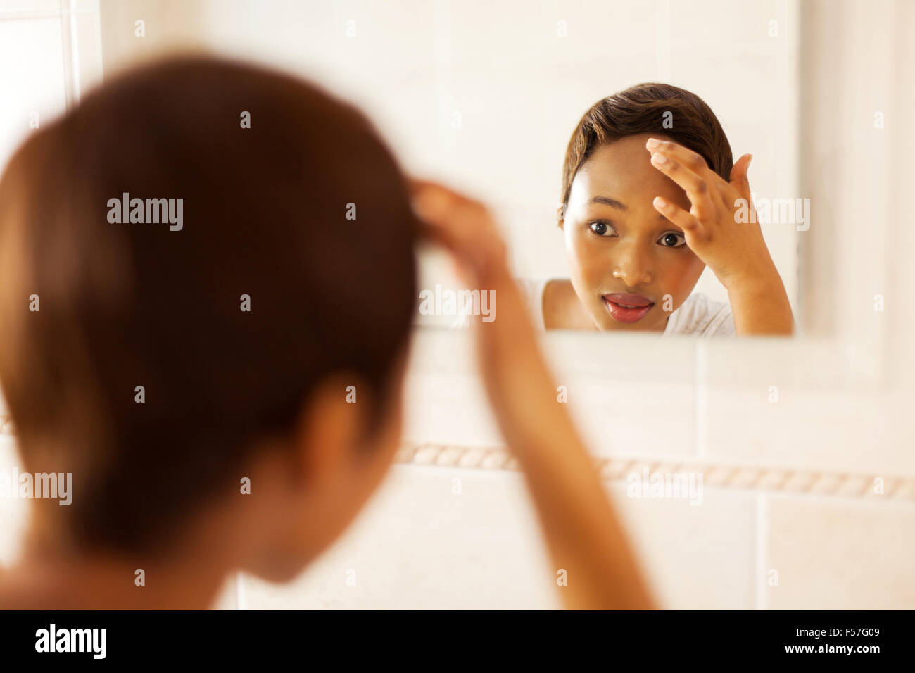 African girl contrôler son visage à la recherche de bouton dans le miroir Banque D'Images