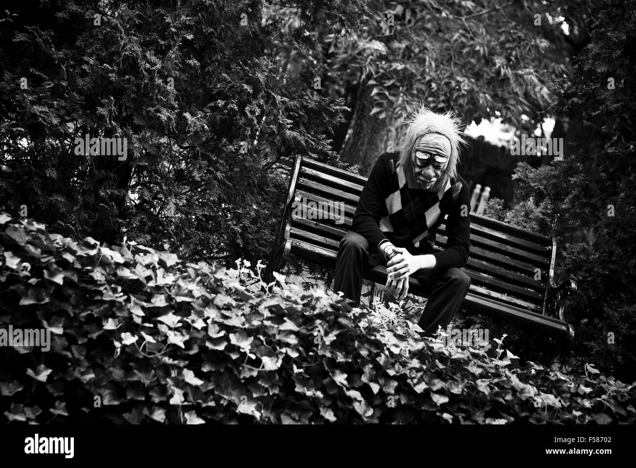 Dans l'homme masque de clown triste assis sur un banc dans le parc Banque D'Images