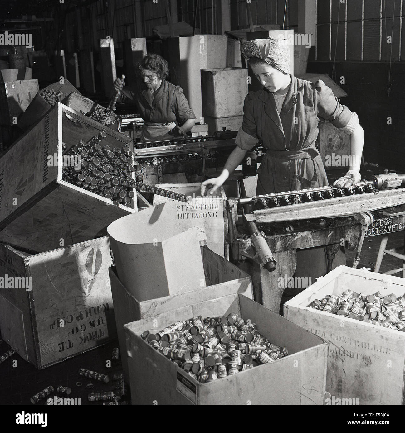 Historique années 1950, femme, ouvrier d'usine de pièces industrielles mettant sur une courroie de convoyeur sur l'usine. Banque D'Images