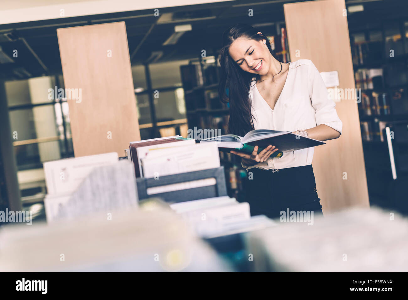 Belle femme lisant des livres dans une bibliothèque et souriant Banque D'Images