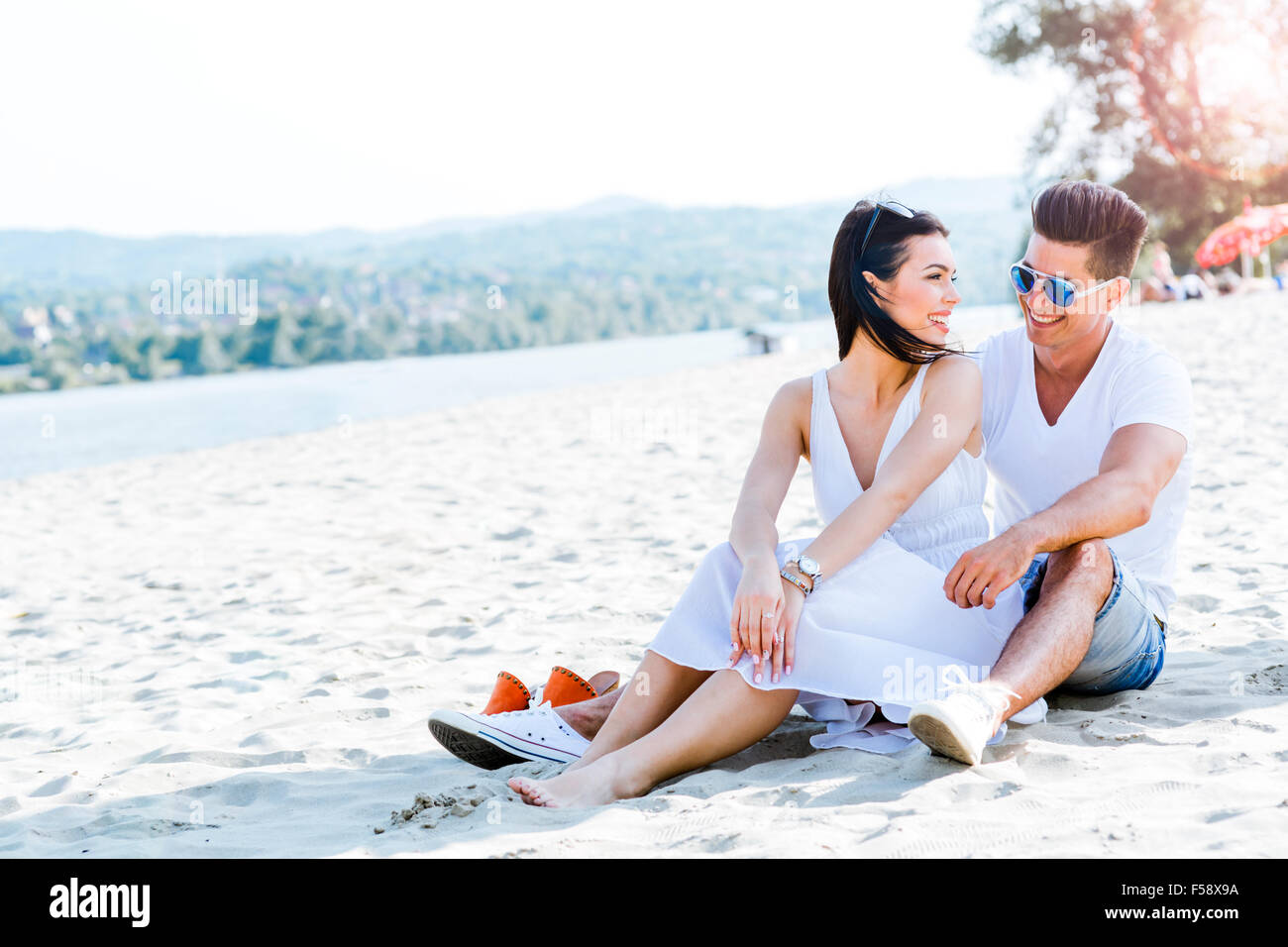 Couple amoureux assis à une plage de sable fin et souriant Banque D'Images