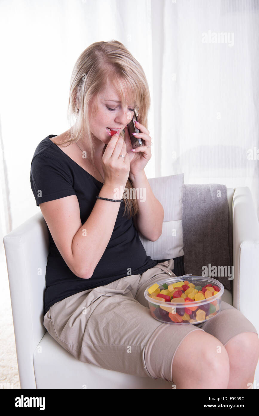 Jeune femme au téléphone manger des douceurs Banque D'Images