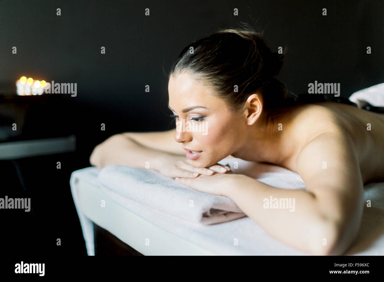 Portrait d'une jeune et belle femme reposant, avec les yeux ouverts sur une table de massage dans une pièce sombre avec des bougies Banque D'Images