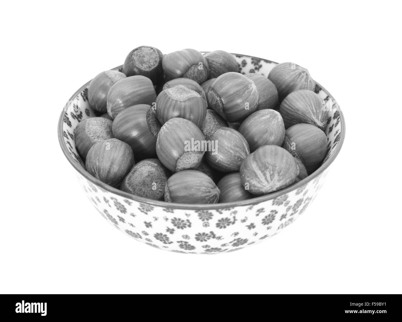 Les noisettes en coque, dans un bol en porcelaine avec un motif fleuri, isolé sur fond blanc - traitement monochrome Banque D'Images