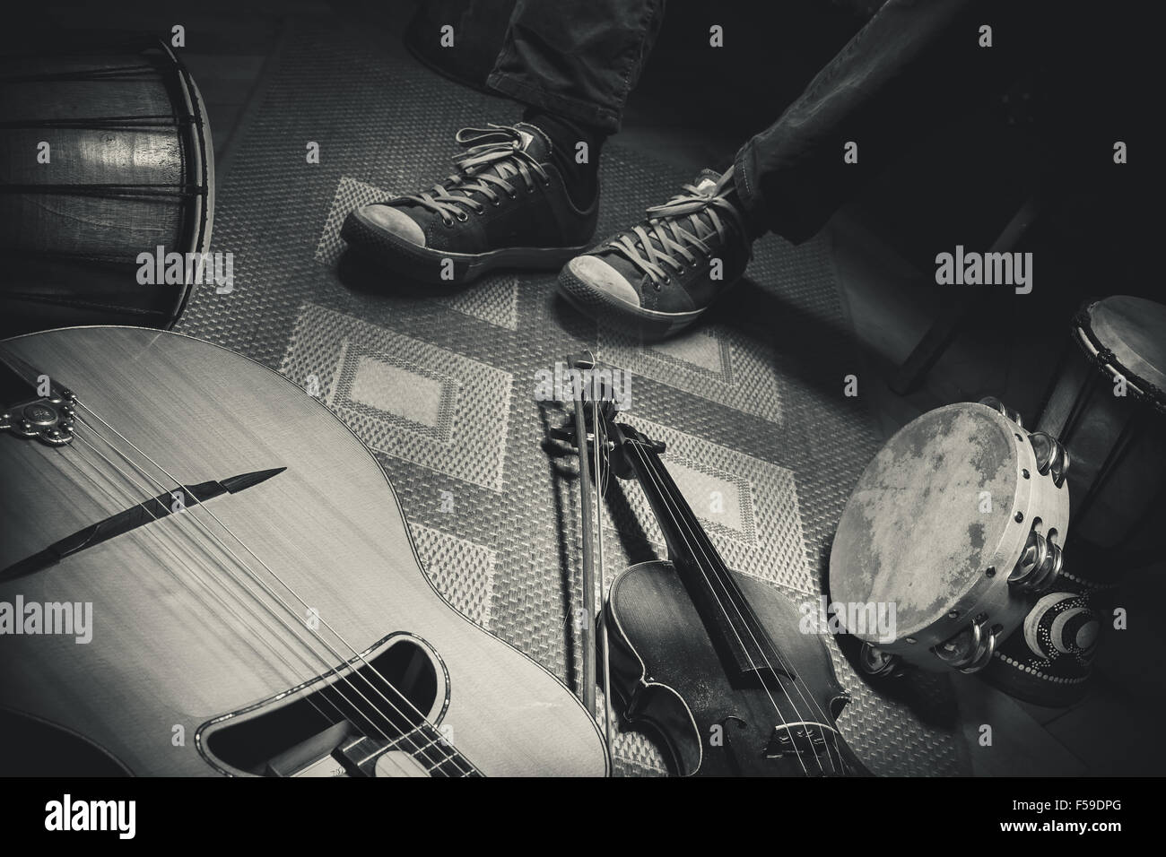 Les jambes d'un musicien et d'instruments acoustiques sur marbre, violon, guitare et percussions, en noir et blanc comme style rétro. Banque D'Images